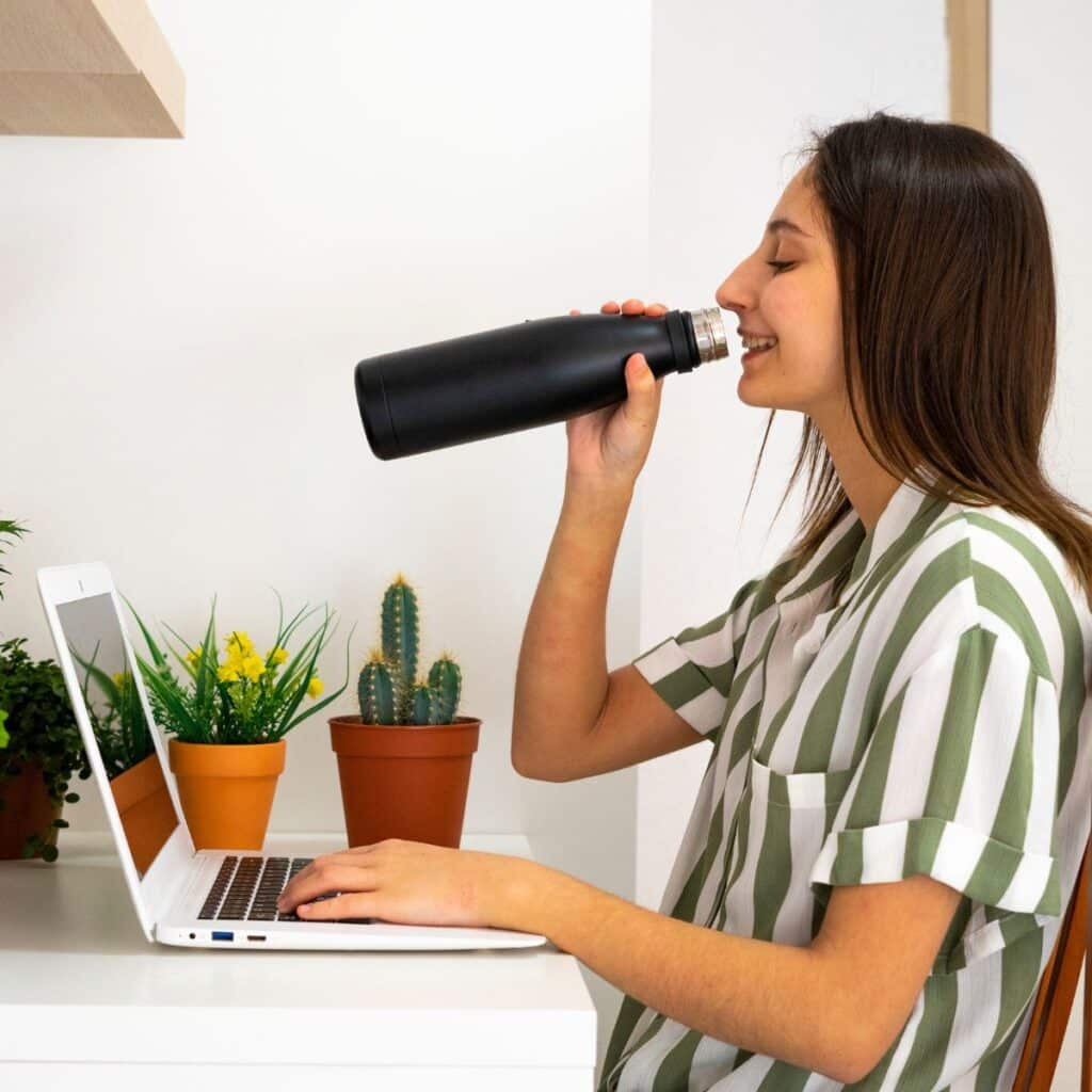 woman drinking water out of a stainless steel mug