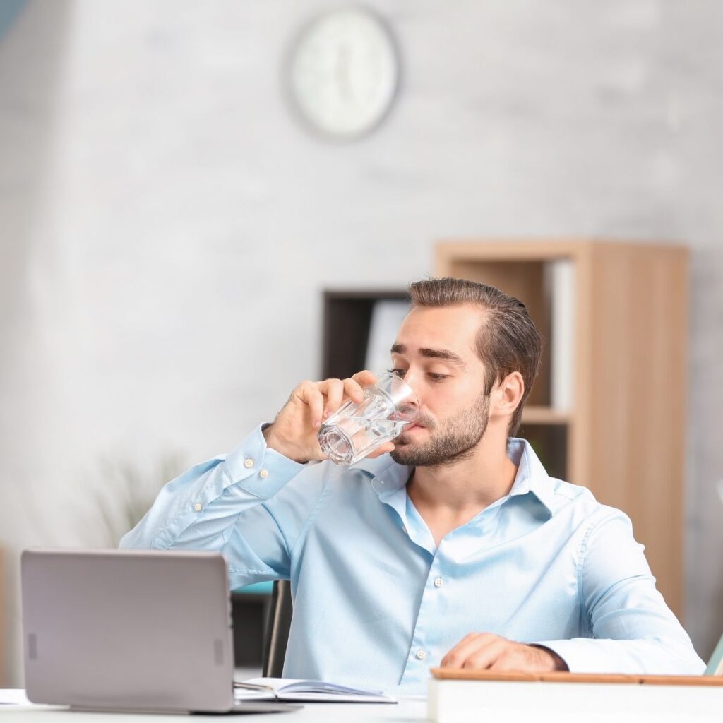 man drinking a glass of water while sitting at his computer