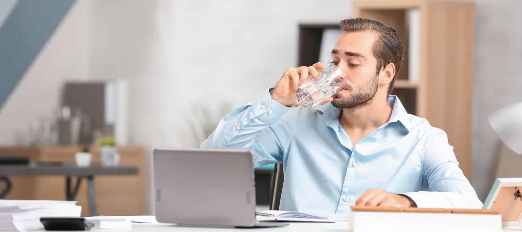 man drinking water out of a glass at his computer