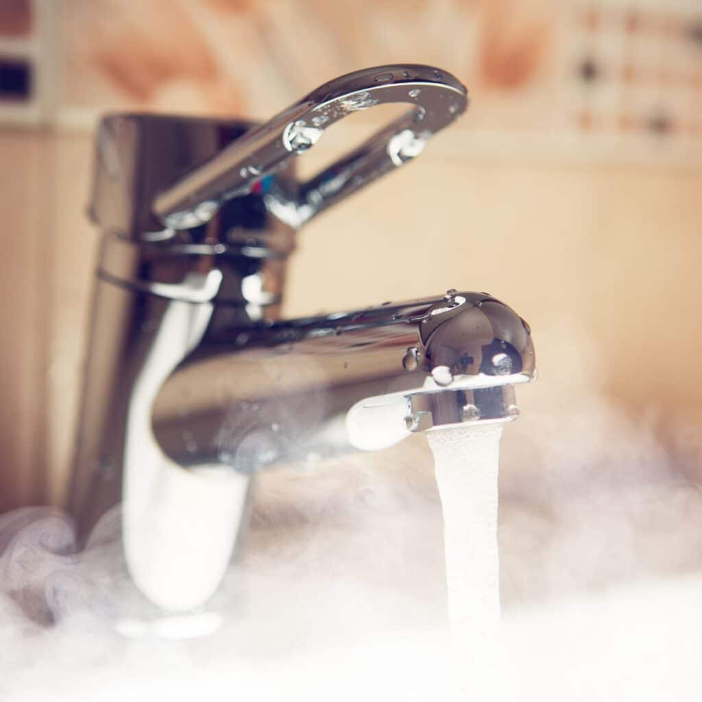 closeup of a faucet on a sink pouring out hot steamy water